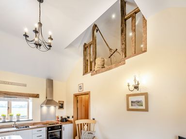 A kitchen with a stove, sink, window with plants, wooden chair, chandelier, and rustic loft railing with farming tools at The Granary in Llanfair Caereinion near Welshpool