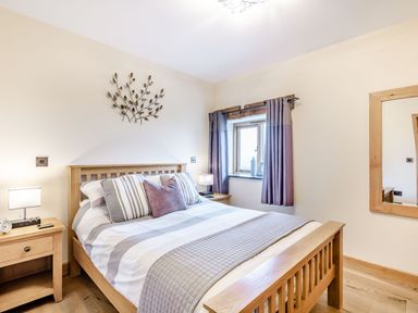 A bedroom with a wooden bed frame bedside tables and a window with curtains at The Granary in Llanfair Caereinion near Welshpool