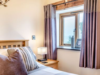A bedroom with a wooden bed a bedside table lamp and a window with curtains at The Granary in Llanfair Caereinion near Welshpool