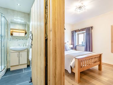 A bedroom with a wooden bed and a window next to a bathroom with a sink and shower at The Granary in Llanfair Caereinion near Welshpool