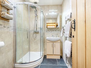 A bathroom with a curved glass shower enclosure a sink with a cabinet a mirror and towels on racks at The Granary in Llanfair Caereinion near Welshpool