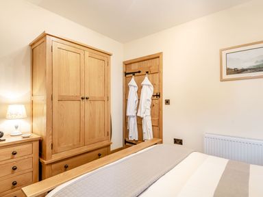 A bedroom with wooden wardrobe chest of drawers bed with gray blanket and bathrobes hanging on wooden door at The Granary Llanfair Caereinion near Welshpool