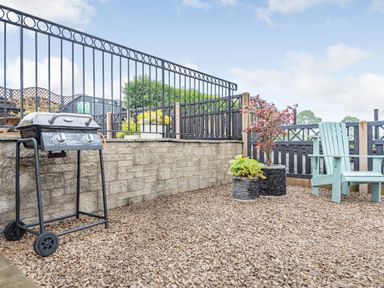 An outdoor patio with a barbecue grill two potted plants and a blue wooden chair at The Granary in Llanfair Caereinion near Welshpool