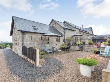 An outdoor patio area with stone buildings sun loungers umbrellas and potted plants at The Granary in Llanfair Caereinion near Welshpool