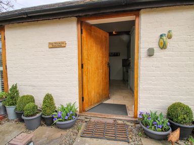 An entrance with a wooden door open revealing a kitchen inside several potted plants around the doorway on a stone and gravel ground at The Milking Parlour in Yarpole near Leominster