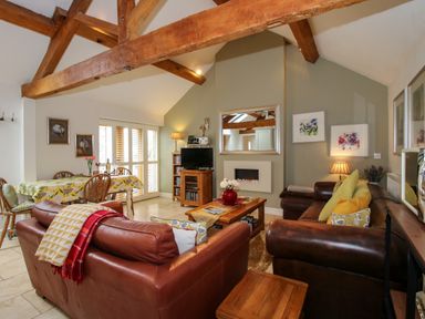 A living room with leather sofas, wooden beams, a coffee table, a dining table with chairs, and a TV at The Milking Parlour Yarpole near Leominster