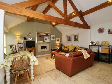 A living room with a dining table wooden chairs leather sofa fireplace and exposed wooden beams at The Milking Parlour in Yarpole near Leominster