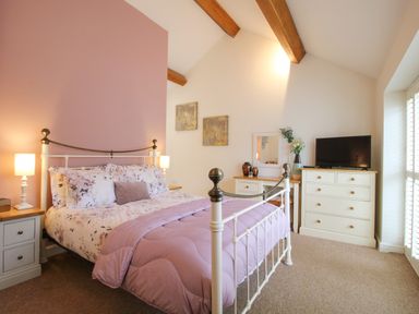 A bedroom with a metal bed floral bedding bedside tables lamps a dresser and a television at The Milking Parlour in Yarpole near Leominster