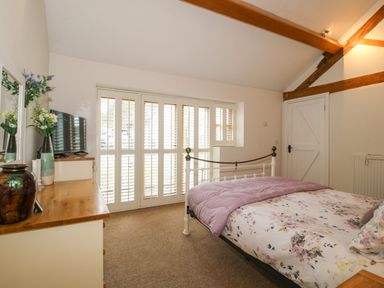 A bedroom with a bed a dresser with a television and flowers and wooden beams on the ceiling at The Milking Parlour in Yarpole near Leominster