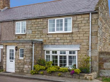Stone house with white framed windows and a white door with plants in front at Sandy Knowes in Low Hauxley near Amble