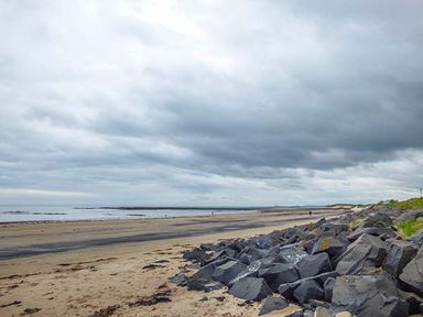 A sandy beach with large rocks on the side and a cloudy sky at Sandy Knowes in Low Hauxley near Amble