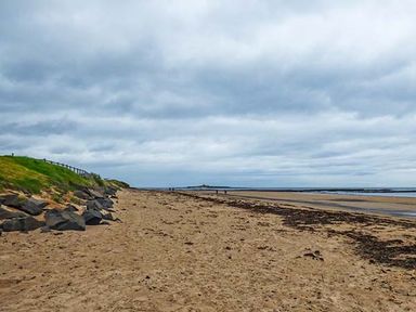 A sandy beach with rocks and grass on the left and the ocean on the right at Sandy Knowes in Low Hauxley near Amble