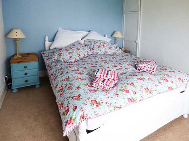 A bedroom with a floral bedspread bed two bedside tables with lamps at Sandy Knowes in Low Hauxley near Amble