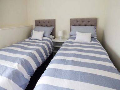 A bedroom with two single beds with striped bedding and a nightstand with a lamp between them at Sandy Knowes in Low Hauxley near Amble