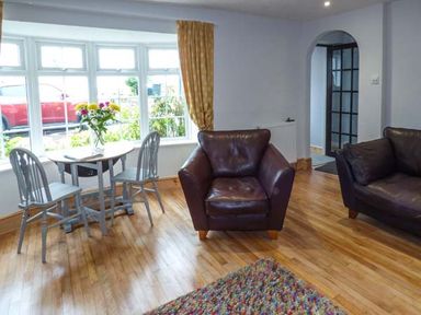 A sitting room with a round table and two chairs by a window and two brown armchairs at Sandy Knowes in Low Hauxley near Amble
