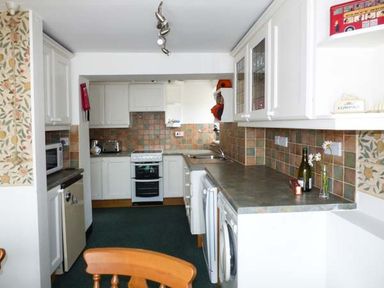 A kitchen with white cabinets tiled backsplash appliances and wooden chair at Sandy Knowes in Low Hauxley near Amble