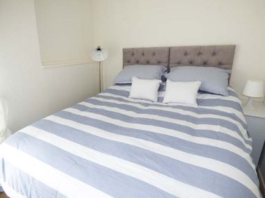 A bedroom with a bed with striped bedding two pillows two cushions and two bedside lamps at Sandy Knowes in Low Hauxley near Amble