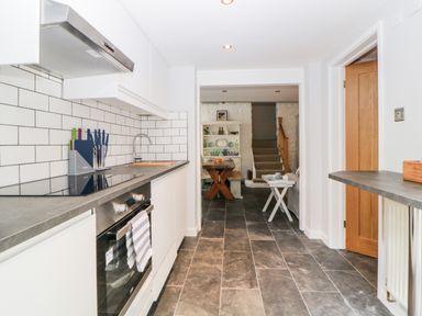 A kitchen with white cabinets and tiled backsplash leading to a dining area with wooden table and stairs at The Old Dairy Maker near Millbrook