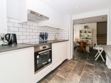 A kitchen with white cabinets black countertop and tiled backsplash next to a dining area at The Old Dairy in Maker near Millbrook