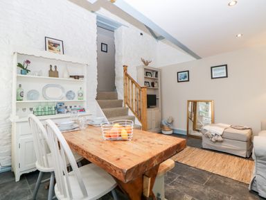 A dining area with wooden table and white chairs next to a staircase and a living room at The Old Dairy Maker near Millbrook