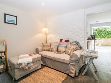 A living room with a sofa and ottoman next to a floor lamp and a small side table with cups at The Old Dairy in Maker near Millbrook