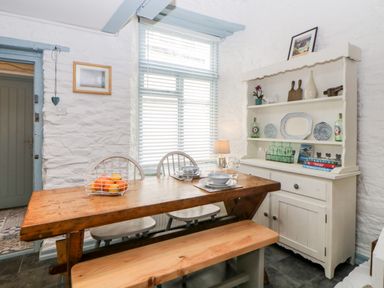 A dining area with a wooden table, chairs, a bench, a cabinet with dishes and books at The Old Dairy Maker near Millbrook