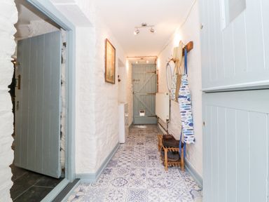 A narrow hallway with patterned tile floor blue doors hooks on the wall and a wooden shoe rack at The Old Dairy Maker near Millbrook