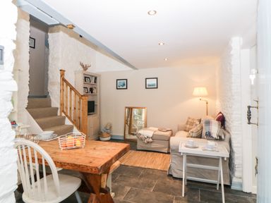 A living area with a wooden dining table, a staircase, a bookcase, a sofa with cushions, a floor lamp, and a mirror at The Old Dairy in Maker near Millbrook