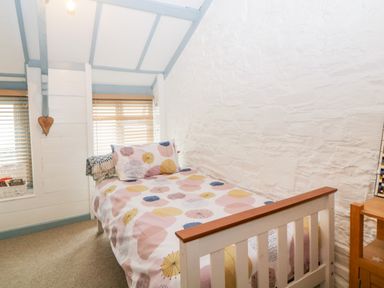 A bedroom with a single bed with patterned bedding a wooden side table and windows with blinds at The Old Dairy Maker near Millbrook