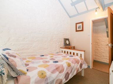 A small bedroom with a single bed with patterned bedding a wooden chair with a framed picture on it and a wooden door open to a hallway at The Old Dairy Maker near Millbrook