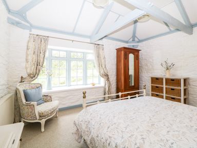 A bedroom with a bed an armchair a wooden wardrobe and a chest of drawers at The Old Dairy Maker near Millbrook