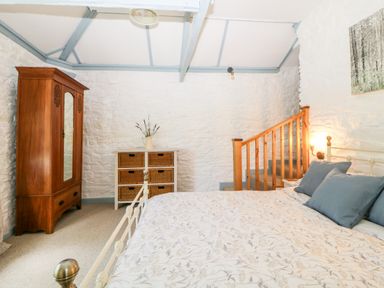 A bedroom with a bed with blue pillows a wooden wardrobe a chest of drawers and wooden stairs at The Old Dairy Maker near Millbrook