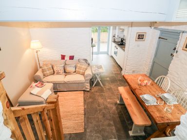 A living area with a sofa and cushions next to a wooden dining table with benches and chairs at The Old Dairy Maker near Millbrook