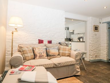 A living room with a beige sofa and pillows next to a floor lamp and a small white table with cups in a home with stone walls at The Old Dairy Maker near Millbrook