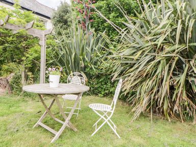 A garden with a wooden round table and two white metal chairs and plants at The Old Dairy Maker near Millbrook