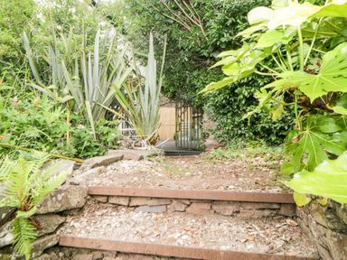 A garden path with stone steps leading to a metal gate surrounded by plants and greenery at The Old Dairy in Maker near Millbrook