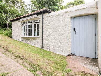 An exterior wall of a stone building with a large window and a blue wooden door at The Old Dairy in Maker near Millbrook