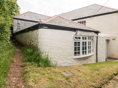 An exterior view of a stone cottage with a pathway and grass at The Old Dairy in Maker near Millbrook