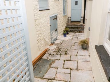 An outdoor patio area with stone flooring white metal table and two chairs potted plants blue doors and cream walls at The Old Dairy Maker near Millbrook