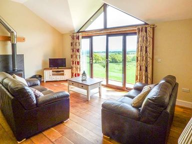 A living room with two black leather sofas a coffee table and a TV near large windows at Black Mountain View in Llanafan Fawr near Builth Wells