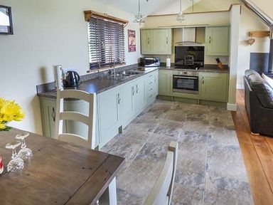A kitchen with green cabinets a black countertop a sink a microwave and a wooden dining table with glasses at Black Mountain View in Llanafan Fawr near Builth Wells