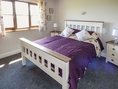A bedroom with a white wooden bed with purple bedding and two bedside tables with lamps at Black Mountain View in Llanafan Fawr near Builth Wells