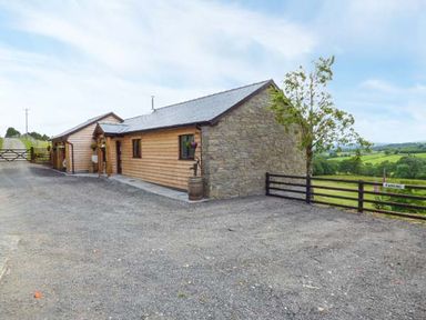 A single story building with wooden and stone walls next to a gravel driveway and green fields at Black Mountain View in Llanafan Fawr near Builth Wells