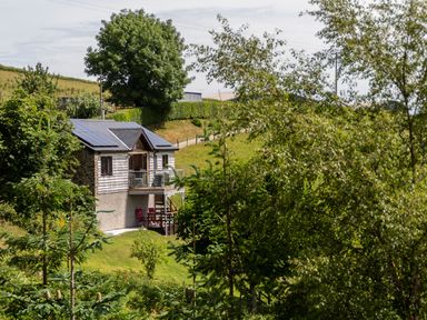 A small house with solar panels on the roof surrounded by trees and grassy hills at Black Mountain View in Llanafan Fawr near Builth Wells