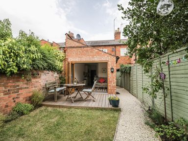 A backyard with a wooden deck and table set beside a brick house at 24 College Lane in Stratford-Upon-Avon