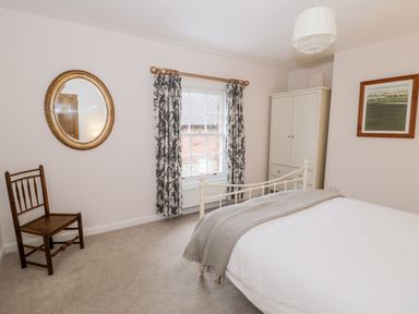 A bedroom with a bed a chair a wardrobe a window with curtains a mirror and a painting at 24 College Lane Stratford-Upon-Avon