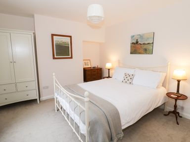A bedroom with a white metal bed frame two bedside tables with lamps a white wardrobe and paintings on the walls at 24 College Lane in Stratford-Upon-Avon