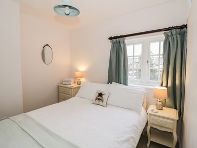 A bedroom with a white bed linens green curtains bedside tables with lamps and an oval mirror on the wall at 24 College Lane in Stratford-Upon-Avon