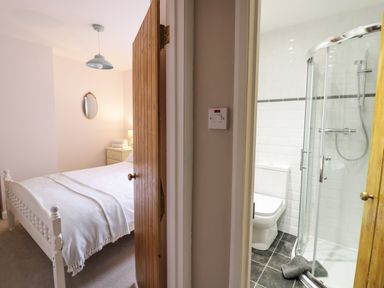 A bedroom with a white bed and a bedside table with a lamp next to a bathroom with a toilet and glass shower at 24 College Lane in Stratford-Upon-Avon