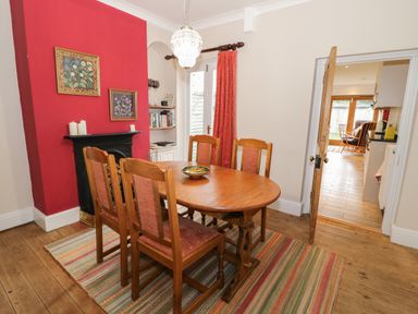 A dining room with a wooden table and four chairs near a red accent wall and a fireplace at 24 College Lane in Stratford-Upon-Avon